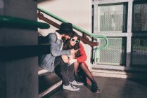 Молодая пара сидит на ступеньках, смотрит на смартфон — стоковое фото