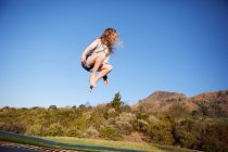 Молодая девушка прыгает на батуте, в воздухе, в сельской местности — стоковое фото
