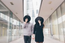 Portrait of young couple in urban environment, holding hands, covering faces with hats — Stock Photo