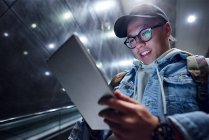 Junger Mann läuft Rolltreppe in U-Bahnhof hinunter und schaut auf digitales Tablet — Stockfoto
