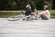 Casal maduro com bicicletas relaxando no cais ao lado do lago — Fotografia de Stock