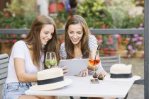 Zwei junge Freundinnen schauen auf digitales Tablet im Bürgersteig-Café — Stockfoto