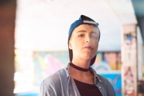 Portrait of young female skateboarder wearing baseball cap and smoking at skateboarding park — Stock Photo