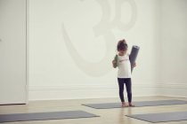 Молода дівчина стоїть в студії йоги, тримаючи йогу килимок — стокове фото