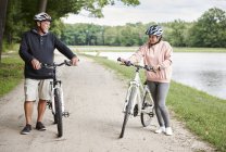Зрелая пара, идущая по сельской дороге на велосипедах — стоковое фото