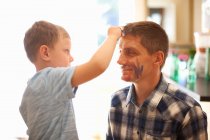 Young boy drawing on father's face using face paint — Stock Photo