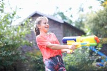 Adolescente chica chorreando pistola de agua en el jardín - foto de stock