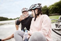Casal maduro em capacetes de bicicleta no cais desfrutando de lanches — Fotografia de Stock