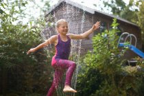 Mädchen springt über Gartensprenger — Stockfoto