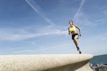 Junge Frau rennt gegen blauen Himmel entlang der Meeresmauer — Stockfoto