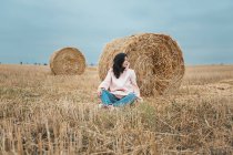 Женщина в розовом плаще сидит у стога сена — стоковое фото