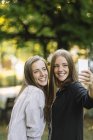 Two young female friends posing for smartphone selfie in park — Stock Photo
