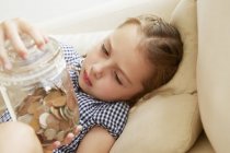 Молодая девушка держит банку денег на диване — стоковое фото