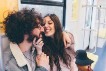 Young couple sitting in subway train, fooling around, woman grabbing man's chin — Stock Photo