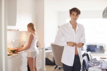 Portrait of man buttoning shirt and pregnant girlfriend in kitchen — Stock Photo