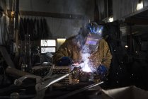 Blacksmith in welding mask working with metal in workshop — Stock Photo