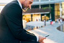 Зрілий бізнесмен сидить на відкритому повітрі зі смартфоном — стокове фото