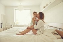 Madre seduta sul letto, abbracciando il bambino — Foto stock