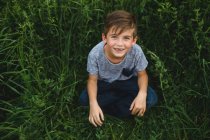 Мальчик смотрит в камеру на зеленом травянистом поле — стоковое фото