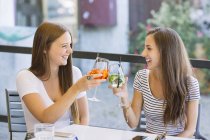 Two young female friends raising a cocktail toast at sidewalk cafe — Stock Photo