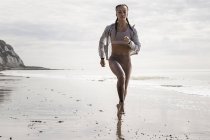 Vista frontale del giovane corridore donna che corre a piedi nudi lungo la spiaggia — Foto stock