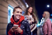 Jovem com smartphone rindo na rua da cidade à noite — Fotografia de Stock