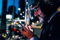Зрілий бізнесмен в мотоциклетному шоломі за допомогою смартфона — стокове фото