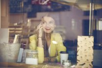 Junge Frau sitzt im Café, benutzt Smartphone, Tätowierungen auf der Hand, Blick durch Café-Fenster — Stockfoto