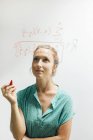 Жінка з червоною маркерною ручкою дивиться на складне рівняння на скляній стіні — стокове фото