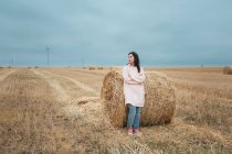 Woman in pink raincoat standing by haystack — Stock Photo