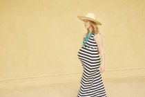 Беременная женщина идет по желтой стене — стоковое фото