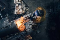 Overhead view of blacksmith shaping red hot metal rod in workshop furnace — Stock Photo