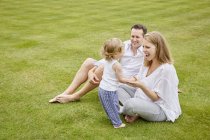 Paar mit Tochter sitzt auf grünem Rasen — Stockfoto