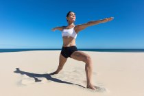 Женщина на пляже с распростертыми объятиями, растягивающаяся в положении йоги — стоковое фото