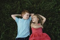 Overhead portrait of boy and sister lying on grass looking at each other — Stock Photo
