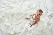 Bambino seduto sul letto, tenendo aperto rotolo di carta igienica — Foto stock