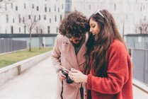 Junges Paar steht draußen, schaut aufs Smartphone, lacht — Stockfoto
