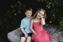Retrato de niño y hermana sentados en la roca - foto de stock