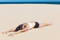 Женщина на пляже, лежащая впереди в позе йоги — стоковое фото