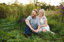 Пара сидящих в высокой траве, улыбающихся — стоковое фото