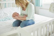 Mother sitting on bed, holding newborn baby — Stock Photo