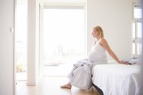 Pregnant young woman sitting on bed — Stock Photo