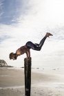 Jovem fazendo suporte de mão com pernas levantadas em postes de praia de madeira — Fotografia de Stock