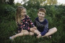 Chica y hermano sentado en el campo - foto de stock