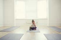 Молодая девушка в студии йоги, сидит на коврике для йоги — стоковое фото
