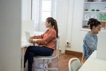 Dos mujeres de negocios escribiendo en computadoras portátiles en el escritorio de la oficina - foto de stock