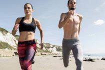Young man and woman running along beach, front  view — Stock Photo