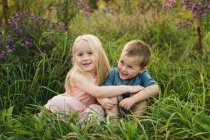 Niño y niña sentados en la hierba alta juntos - foto de stock