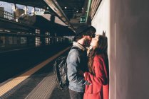 Pareja joven de pie en la plataforma del tren, besando - foto de stock