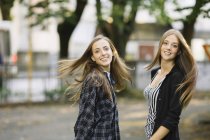 Портрет двох молодих друзів-жінок, що кружляють довге коричневе волосся в парку — стокове фото